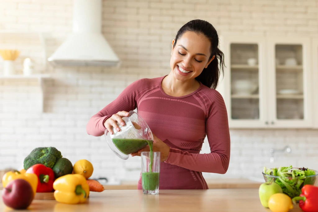 Isabella "Izzy" Rossi smiling as she pours a freshly blended green smoothie from a blender into a glass.