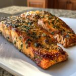 Two glistening, golden-brown fillets of air fryer salmon topped with chopped green herbs resting on a white plate.