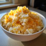 A white bowl filled with fluffy white rice topped generously with melted shredded cheddar cheese, showcasing amazing cheesy rice.