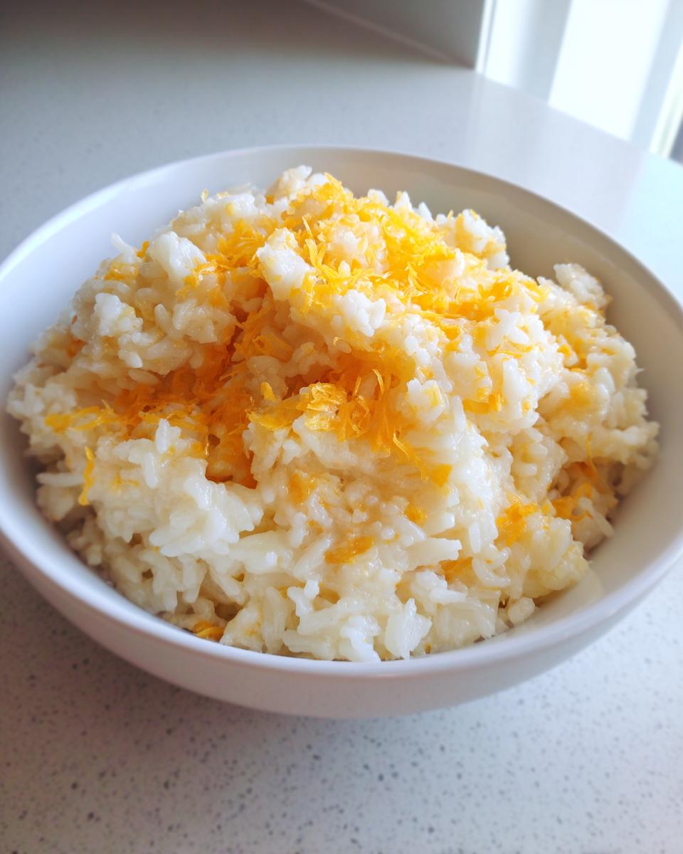A white bowl filled with creamy, white cheesy rice topped generously with bright orange shredded cheddar cheese.