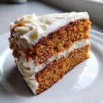 Close-up of a moist slice of carrot cake recipe layered with thick cream cheese frosting on a white plate.