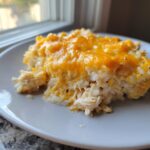 A close-up of a scoop of cheesy chicken and rice casserole topped with melted cheddar cheese.