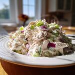 A generous mound of creamy cottage cheese chicken salad mixed with visible chunks of red onion and celery, served on a white plate.