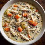 Close-up of creamy chicken wild rice soup with chunks of carrot and celery, garnished with herbs.
