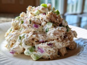 A close-up serving of creamy cottage cheese chicken salad mixed with diced red onion and celery on a white plate.