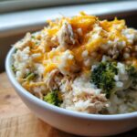 Close-up of a bowl of creamy crock pot chicken and rice mixed with broccoli florets and topped with melted cheddar cheese.