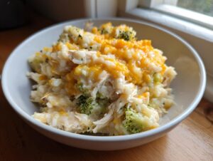 A white bowl filled with creamy crock pot chicken and rice mixed with broccoli and topped with melted cheddar cheese.