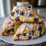 Three delicious blueberry scones stacked on a white plate, drizzled generously with white vanilla glaze.