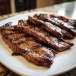 Close-up of juicy, grilled, and sliced steak coated in a rich Carne asada marinade, resting on a white plate.