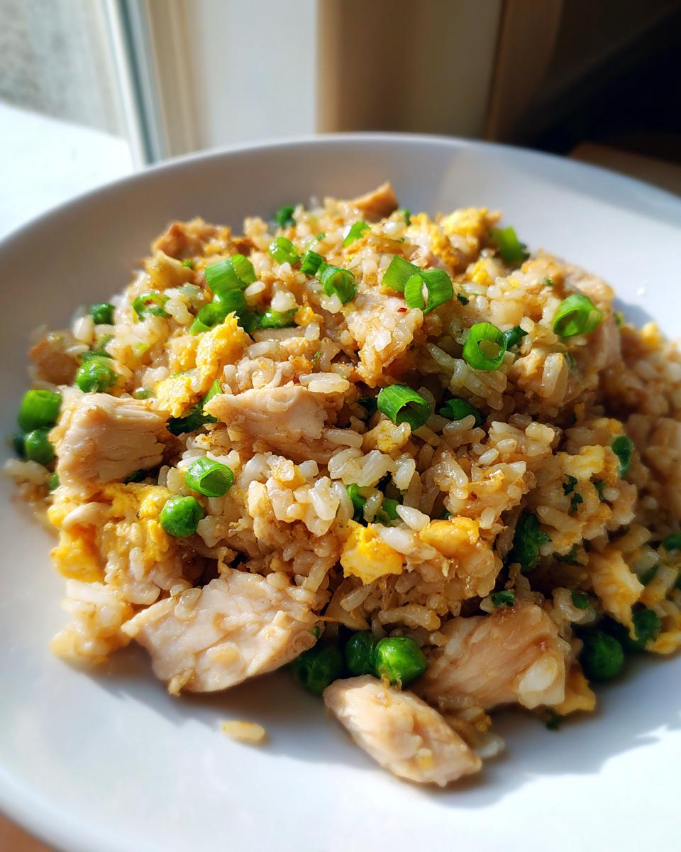 Close-up of delicious chicken fried rice mixed with scrambled egg, green peas, and topped with fresh scallions.