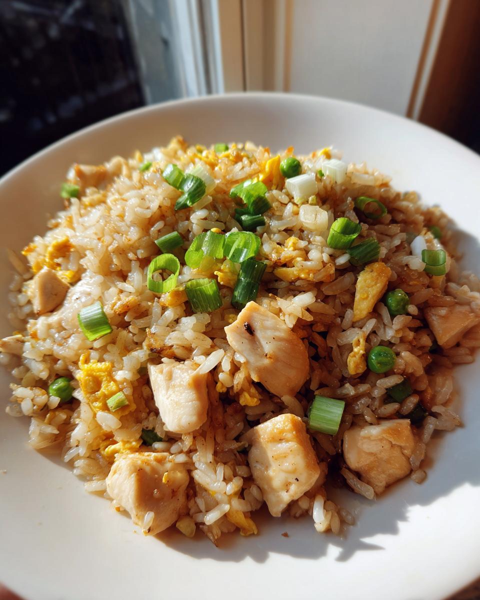 A close-up of a white bowl filled with flavorful chicken fried rice, topped with green onions.