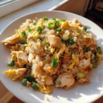 Close-up of homemade chicken fried rice with chunks of chicken, scrambled egg, and green onions on a white plate.