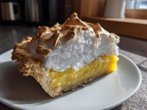 A close-up of a slice of lemon meringue pie showing the thick, fluffy, torched meringue topping over bright yellow lemon curd.