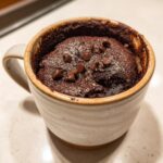 Close-up of a rich, dark chocolate mug cake topped with chocolate chips, ready to eat.