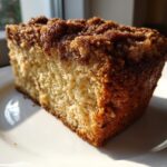 Close-up of a moist slice of coffee cake featuring a thick, dark brown cinnamon streusel topping.