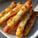 Close-up of several golden brown, soft breadsticks topped with melted cheese, garlic, and parsley.