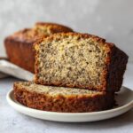 Two thick slices of moist sugar free banana bread stacked on a white plate, showing the speckled texture.