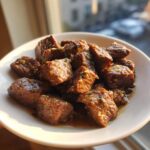 Close-up of tender, cubed crockpot steak pieces coated in a savory garlic sauce on a white plate.