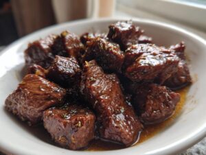 Close-up of tender, cubed crockpot steak pieces coated in a rich, glossy brown sauce with herbs.