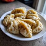 A close-up of several freshly steamed Traditional Chinese Dumplings arranged on a white plate.