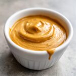 Close-up of thick, creamy peanut sauce swirled in a small white ramekin, ready for dipping.