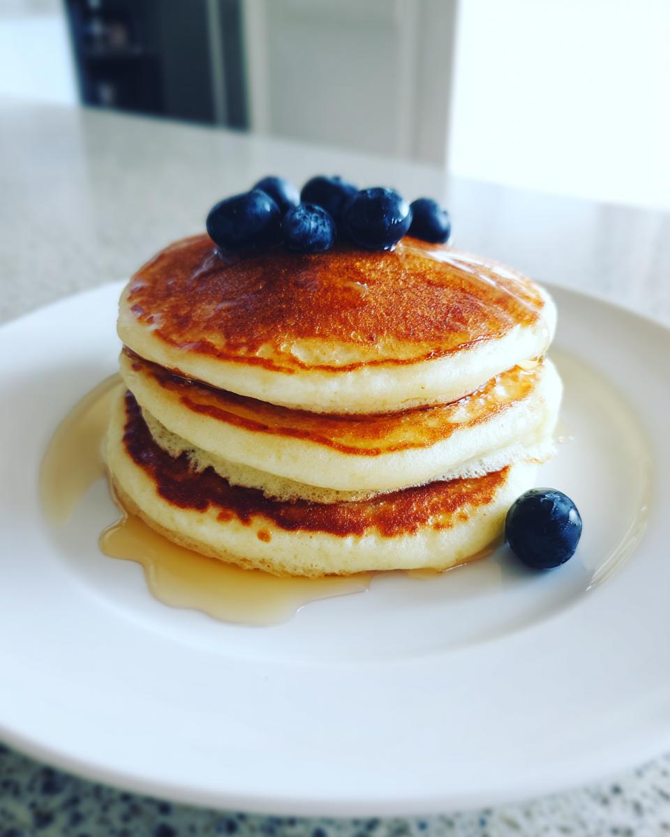 A stack of three golden brown almond flour pancakes topped with fresh blueberries and drizzled with syrup.