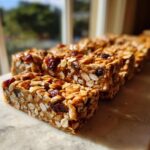 Close-up of several chewy no bake granola bars packed with oats and dried cranberries, set against a bright window.