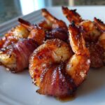 Close-up of perfectly cooked, glazed bacon wrapped shrimp on a white plate.