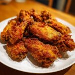 A close-up of a pile of perfectly crispy, golden brown fried chicken wings served on a white plate.