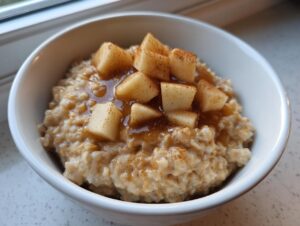 Close-up of a white bowl filled with creamy apple cinnamon oatmeal, topped with diced apples, syrup, and cinnamon.
