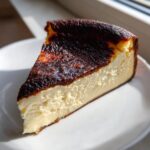 A perfect slice of creamy Basque cheesecake with a deeply caramelized, burnt top resting on a white plate.