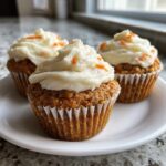 Three delicious carrot cake muffins topped with thick cream cheese frosting and orange sprinkles.