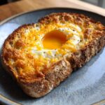 Close-up of cheesy egg toast featuring a perfectly cooked egg with a runny yolk nestled in melted cheddar cheese on thick toast.