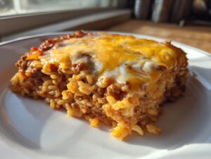 Close-up of a hearty slice of mexican rice casserole topped with melted cheddar cheese, served on a white plate.