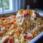 A spoonful of creamy, cheesy monterey chicken spaghetti being lifted from a baking dish, showing cheese pull and crispy topping.