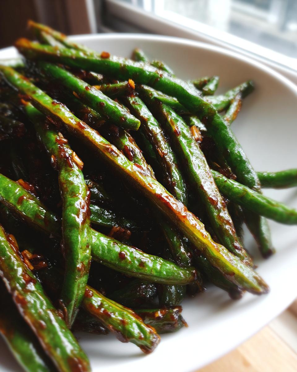 A close-up of vibrant green beans coated in a savory, dark garlic sauce, ready to serve.