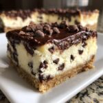 A close-up view of a rich chocolate chip cheesecake bar with a graham cracker crust, topped with chocolate ganache and mini chips.