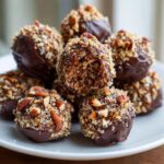 A stack of rich, chocolate-dipped pecan pie balls generously coated in chopped pecans.