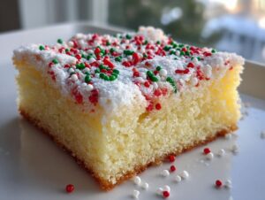 A close-up of a square slice of Christmas gooey butter cookies topped with white frosting and red, green, and white holiday sprinkles.