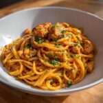 Close-up of a bowl filled with creamy cajun chicken pasta, featuring linguine coated in orange sauce and topped with diced chicken and parsley.