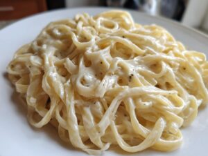 Close-up of fettuccine pasta generously coated in rich, creamy homemade alfredo sauce with visible black pepper flecks.