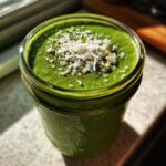 Close-up of creamy matcha chia pudding in a glass jar, topped with shredded coconut flakes.