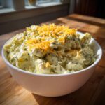 A white bowl filled with creamy pickle dip, mixed with green herbs and topped with shredded cheddar cheese.