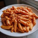 A close-up of penne pasta generously coated in creamy pink sauce pasta, topped with black pepper.