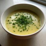 A close-up of a bowl of creamy, yellow potato leek soup garnished generously with freshly chopped green chives.