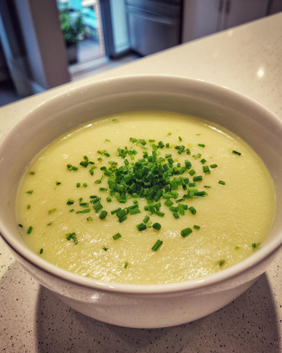 A close-up of a bowl of creamy potato leek soup garnished generously with freshly chopped green chives.