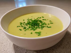 A close-up of a bowl of creamy, pale yellow potato leek soup topped with freshly chopped green chives.