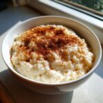 A close-up of creamy rice pudding served in a white bowl, generously topped with ground cinnamon.