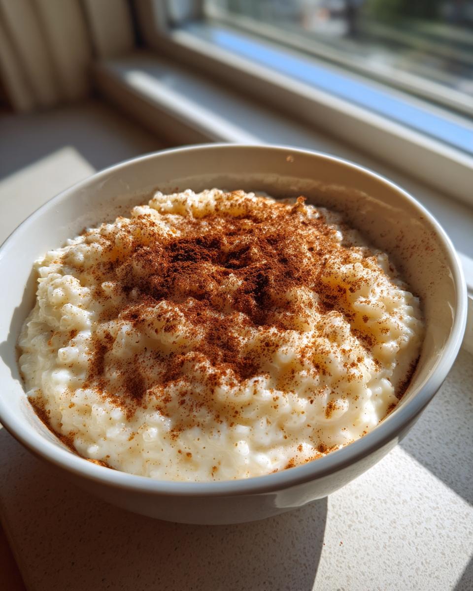 A close-up of creamy rice pudding topped generously with ground cinnamon in a white bowl.
