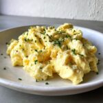 A close-up of creamy, soft scrambled eggs topped with fresh chives and black pepper.